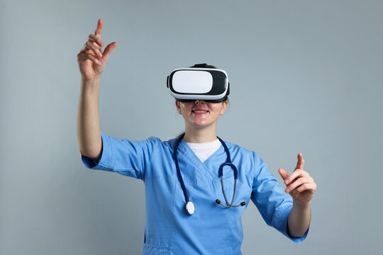 Modern technology. Doctor in headset using virtual screen on grey background