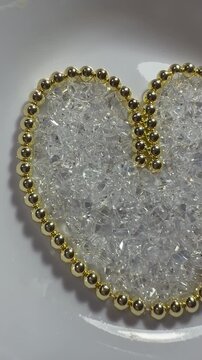 A heart made of polished golden hematite beads with shimmering triangular glass beads inside. Sparkling, jewelry-grade materials perfect for craft, design, and holiday themes