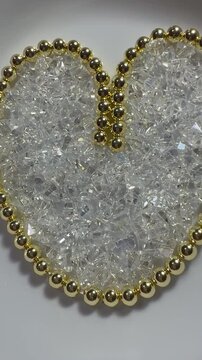 A heart made of polished golden hematite beads with shimmering triangular glass beads inside. Sparkling, jewelry-grade materials perfect for craft, design, and holiday themes