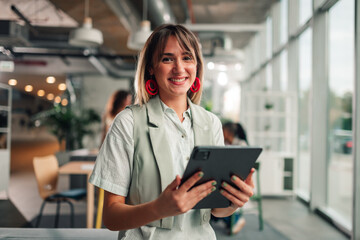 Young businesswoman smiling, holding tablet in modern office