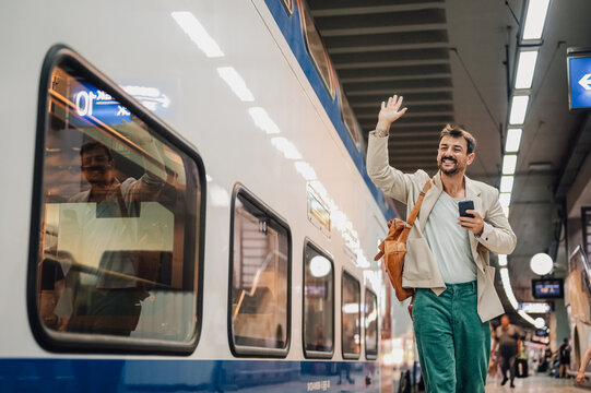 Man waving goodbye at train station platform - Powered by Adobe