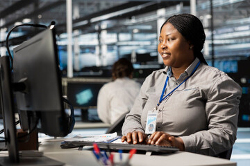 Data center system administrator uses PC to update servers tech, configuring gear using software. African american server farm worker reviewing hardware analytics, ensuring reliable network operations