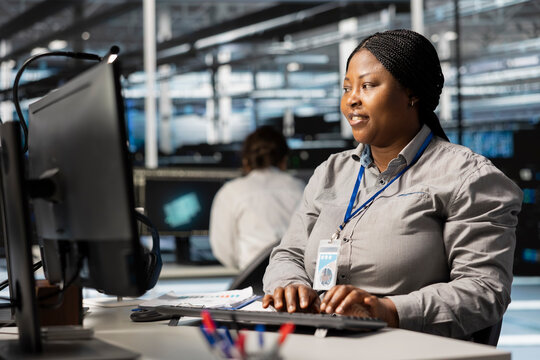 Data center system administrator uses PC to update servers tech, configuring gear using software. African american server farm worker reviewing hardware analytics, ensuring reliable network operations