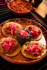 Panuchos, a typical dish from Yucatan, Mexico. A handmade, fried corn tortilla filled with beans, topped with cochinita pibil, pickled red onion, and habanero pepper.