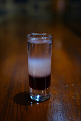 Colorful layered cocktail shot glass with orange, dark, and light layers surrounded by melting ice cubes on dark glossy bar surface, perfect for nightlife and party themes. High quality photo