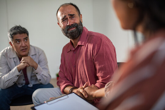 Adult men in group therapy, crying and receiving support