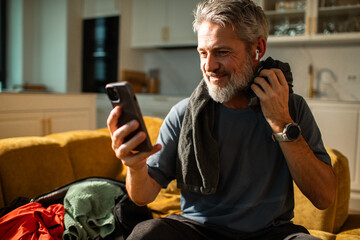 Mature man smiling with smartphone after workout at home
