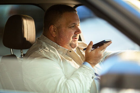 Adult man using voice assistant while driving in car, focused