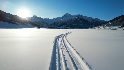 Cross-country ski tracks winding across a vast pristine snowfield towards sunlit mountains for a winter adventure concept and peaceful journey - Powered by Adobe