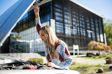 Woman examining broken down car engine problem
