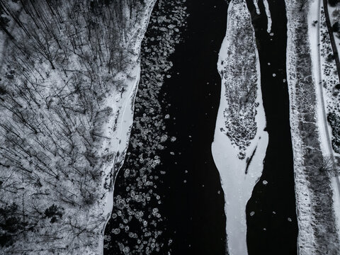 Aerial view of the Neris River's icy grip contrasts the snow-laden banks, a monochrome landscape where nature's artistry etches frozen patterns, Vilnius, Vilnius, Lithuania.