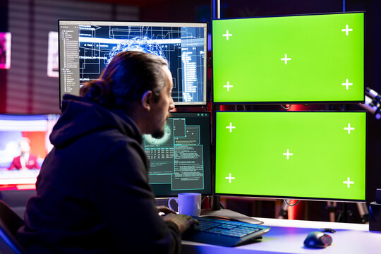 Hacker using artificial intelligence tech on green screen PC to steal credit card numbers and infiltrate banking systems. Rogue engineer in secret hideout running malicious code on chroma key computer