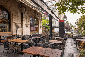 Outdoor café terrace with modern furniture, wooden tables, woven chairs, and large awnings