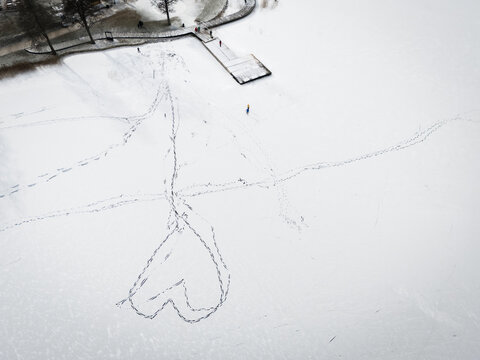 Aerial view of a heart shape traced in the snow-covered frozen lake near a small pier, Trakai, Trakai, Lithuania. - Powered by Adobe