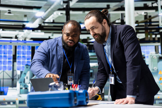Diverse team of engineers and technicians collaborate in a solar panel factory, reviewing blueprints and sharing ideas to enhance renewable energy production and sustainable innovation.