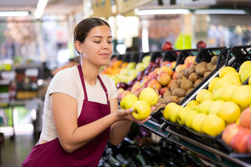 Young woman seller in apron lays out apples in supermarket