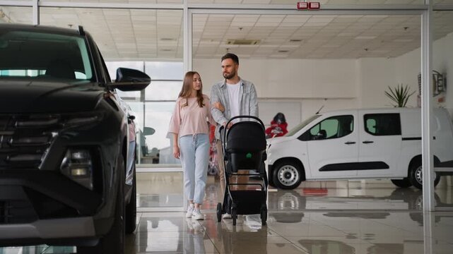 Young family with baby stroller choosing new car at dealership
