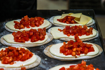 Fresh flatbreads arranged on a tray, each covered with creamy sauce and topped with chopped tomatoes or paprika mix at a holiday street food market.
