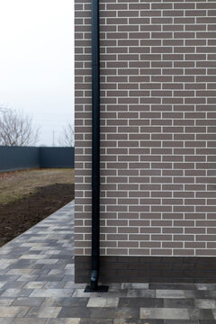 Black rain gutter downspout on dark brick house corner with pavement