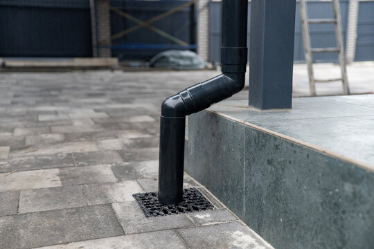 Black gutter system downspout connecting to ground drainage grate