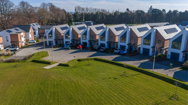 Aerial view of modern houses with sharply angled roofs and solar panels casting long shadows across manicured lawns, Exeter, England, United Kingdom.