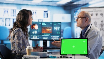 Senior medic talking to his female patient next to mockup green screen, medical consultation on health insurance. Old woman with a disease discussing with physician about medicine. Camera A.