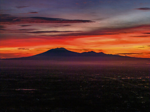 Aerial view of a horizon ablaze with fiery hues, silhouetting the majestic Mount Lawu against a vibrant sunrise, Klaten Regency, Central Java, Indonesia.
