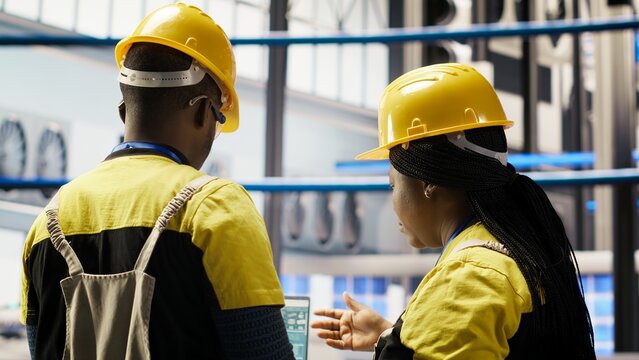 Smart factory engineering team using laptop to analyze IoT sensors data, refining equipment efficiency. Teamworking industrial plant colleagues perform system diagnostics to reduce downtime, camera B