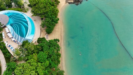 Aerial view of a serene coastline meeting lush greenery, with a striking blue pool contrasting against the sandy beach, Phuket, Phuket, Thailand.