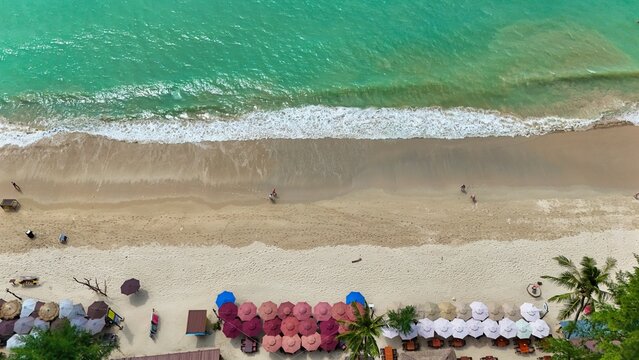 Aerial view of the beach with people strolling along the shore as the waves gently crash, umbrellas lined up in rows along the beach, Phuket, Phuket, Thailand.