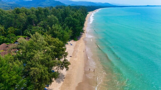 Aerial view of the turquoise sea gently kissing the sandy shore, fringed by verdant trees, offering a tranquil escape, Phuket, Phuket, Thailand.