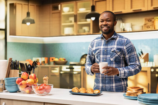 Portrait of African American man serving a healthy breakfast with pastry and coffee, standing at the kitchen counter. Young adult showing focus on homemade food for the morning routine. - Powered by Adobe