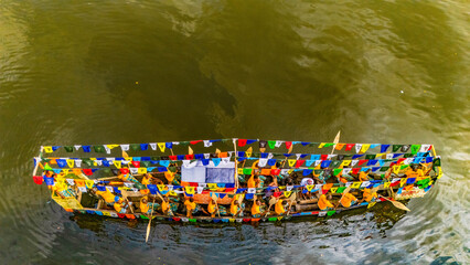 Aerial view of a vibrant boat adorned with colorful flags and people in yellow, gliding across the water, Buguma, Rivers State, Nigeria.