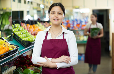 Friendly asian woman seller in apron stands with arms crossed on chest and waits for customers.Vegetable shop at home,hypermarket,supermarket vegetable department