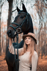 Obraz premium Woman stands with a horse in a forest during autumn while touching its face gently