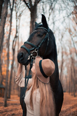 Obraz premium Woman stands with a horse in a forest during autumn while touching its face gently