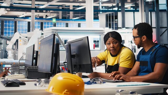 Employees work on photovoltaic design updates in clean energy plant, reducing downtime for operational efficiency in a solar panel factory. Black team of engineers fixing technical issues. Camera B.
