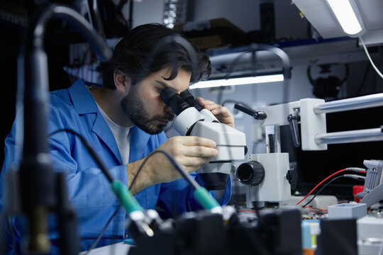Technician working on circuit board under microscope in lab