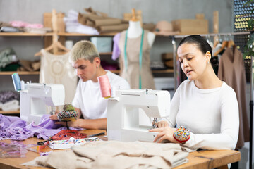 Two attentive male and female dressmakers working with sewing-machine in tailor's workshop
