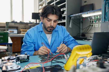 A man worker dressed in a blue coat is focused on working with a motherboard
