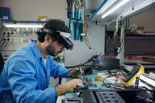 A man soldering technician in a blue lab coat works on electronics and devices
