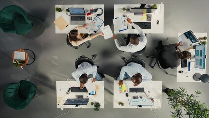 Top down view of diverse coworkers analyzing business data and metrics during report sharing session in boardroom. Professional work team discuss forecasting and management insights.