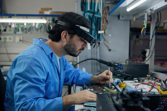 Technician man soldering technician dressed in a blue lab coat is diligently repairing a laptop