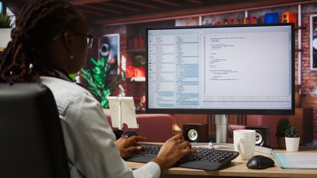 Programmer at computer desk coding, creating software, implementing algorithms. African american IT specialist in home office working with code editor, building applications, camera A