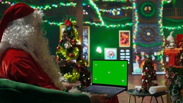 Santa Claus making list of kids who has been naughty or nice on green screen laptop. Person preparing travel plans on chroma key notebook before visiting children, camera A