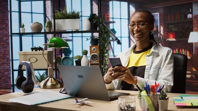 Portrait of cheerful person reading messages on mobile phone, delighted after receiving good news. Joyous woman in cozy apartment excited by SMS on smartphone, chatting with friends, camera A