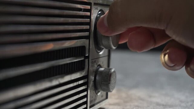 Person tuning an old analog radio, hand rotating dial on vintage device, capturing nostalgic sound searching and classic frequency adjustment.
