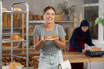 Interested Muslim female customer looks around in baker's and saleswoman doing her work in background