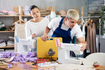 Asian woman dressmaker called a master to repair a sewing machine. Mechanic repairs a sewing...