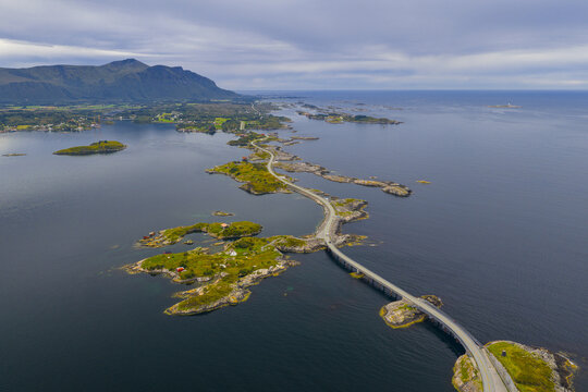 Aerial view of the winding Atlanterhavsveien, a ribbon of grey concrete cutting through the dark blue sea, connecting verdant islands under a moody sky, Averoy, More og Romsdal, Norway.